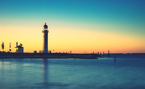 Lighthouse on sea against sky during sunset