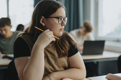 Thoughtful teenage girl with long brown hair sitting in classroom