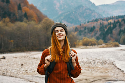 Portrait of smiling young woman standing against mountains