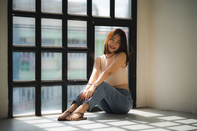 Portrait of young woman sitting on window at home