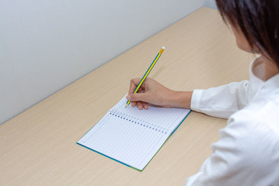 Midsection of woman writing in book on table