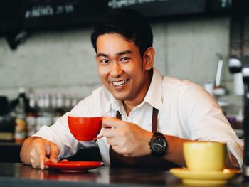 Portrait of smiling barista holding coffee cup on table in cafe