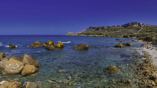 Rocks in sea against clear blue sky