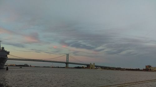 Suspension bridge over river against cloudy sky