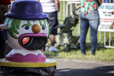 Close-up of clown garbage can with people standing in background