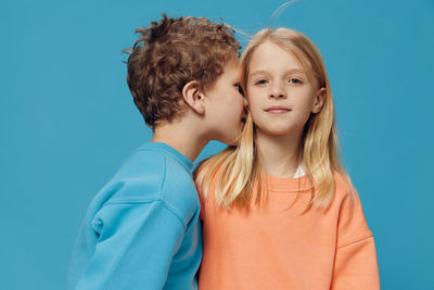 Brother whispering in sisters ear against blue background