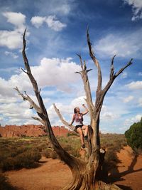 Woman sitting on bare tree at desert