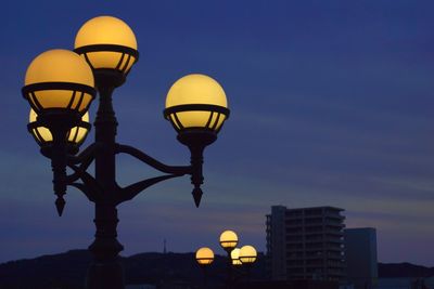 Low angle view of illuminated street light against building at dusk