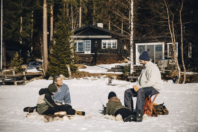 Smiling mature men with boys ice fishing on snow during sunny day