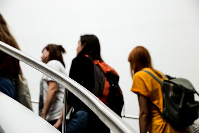 Rear view of people standing by railing against sky