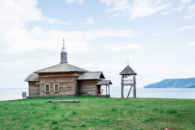 An old wooden log house russian house and a bell tower on the bank of the river on a summer day