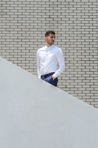 Young man with hands in pockets standing on steps against wall