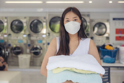 In the self-service laundry with dryer machines in the backdrop, a young woman enjoys clean ironed.