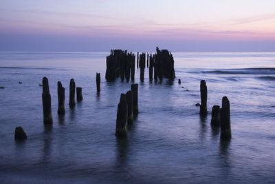 Wooden posts in sea against sky during sunset