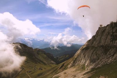 Person paragliding over mountains against cloudy sky