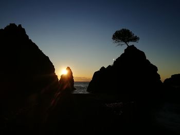 Silhouette rocks by sea against sky during sunset