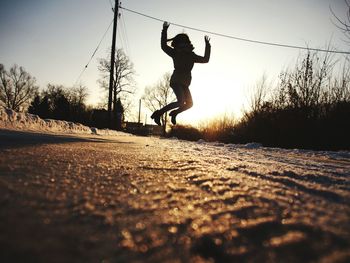 Woman jumping on road during sunset