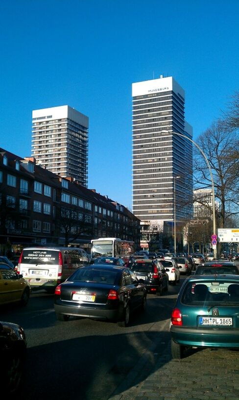 building exterior, architecture, transportation, built structure, car, city, land vehicle, mode of transport, street, clear sky, road, traffic, city life, city street, skyscraper, building, office building, modern, blue, on the move