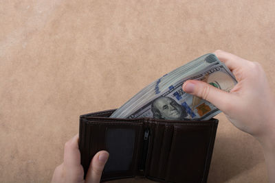 Cropped hand inserting paper currencies in wallet on table