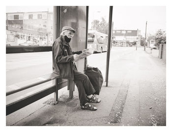 Full length of man sitting on bench in city