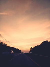 Cars moving on road against cloudy sky during sunset