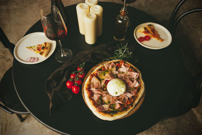 High angle view of neapolitan pizza with burrata and ham served on black table