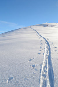 Tire tracks on snow covered land against blue sky