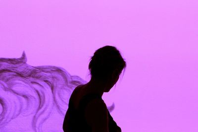 Side view of woman standing against pink wall