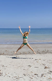 Full length of woman jumping at beach against clear sky