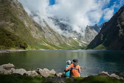 Rear view of man looking at lake by mountains against sky