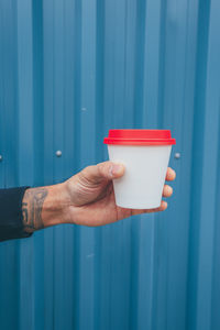 Cropped hand holding coffee against blue wall