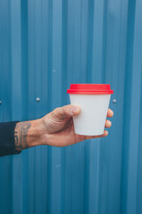 Midsection of person holding red umbrella against blue wall