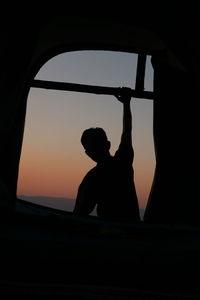 Silhouette man standing by window at sunset