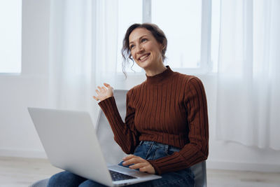 Young woman using laptop while sitting on sofa at home