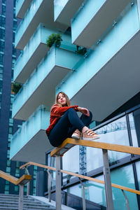 Low angle view of woman sitting on railing against building in city