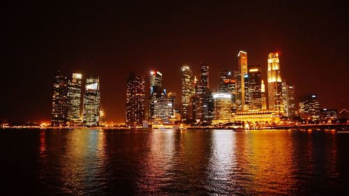 Illuminated city by sea against sky at night