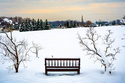 Empty bench on snow covered field against sky during winter