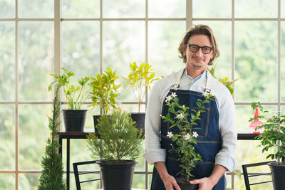 Portrait of smiling young man standing by potted plants