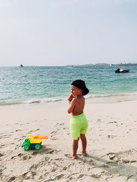 Little tanned boy stay at sandy beautiful beach with toy car, hot day at jbr beach