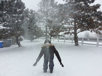 Rear view of person standing on snow covered field against trees