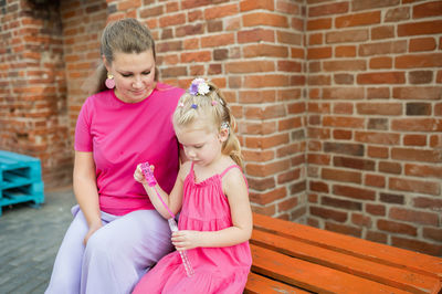 Side view of cute girl blowing bubbles while standing against brick wall