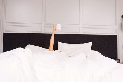Woman holding coffee cup while lying on bed at home