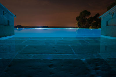 Swimming pool by building against sky at night