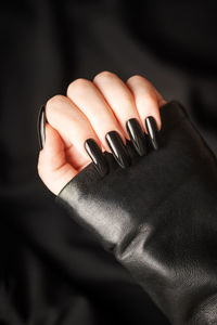 Hands of young girl with black manicure on nails on black background