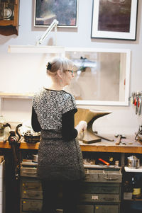 Rear view of female craftsperson standing at workbench in jewelry workshop