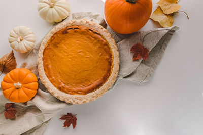 Traditional autumn food, pumpkin pie and colorful pumpkins on the white table, top view