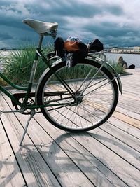 Bicycle on boardwalk by sea against sky