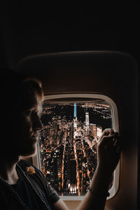 Close-up of man sitting in airplane against illuminated city at night
