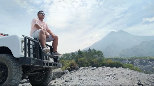 Man sitting on mountain against sky