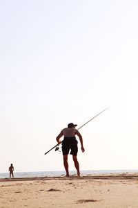 Rear view of man standing on beach against clear sky